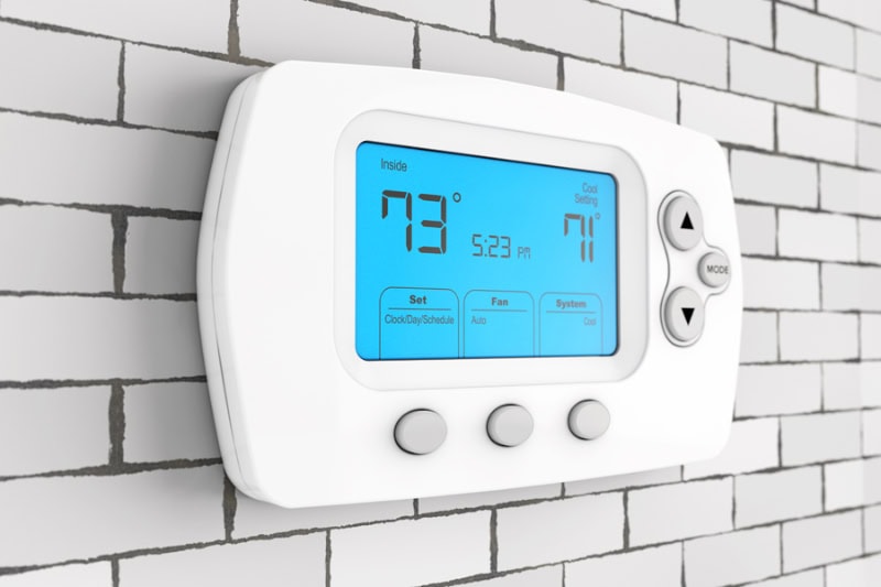 Thermostat Settings: On vs. Auto Photo of a digital thermostat mounted on a wall with a blue light.